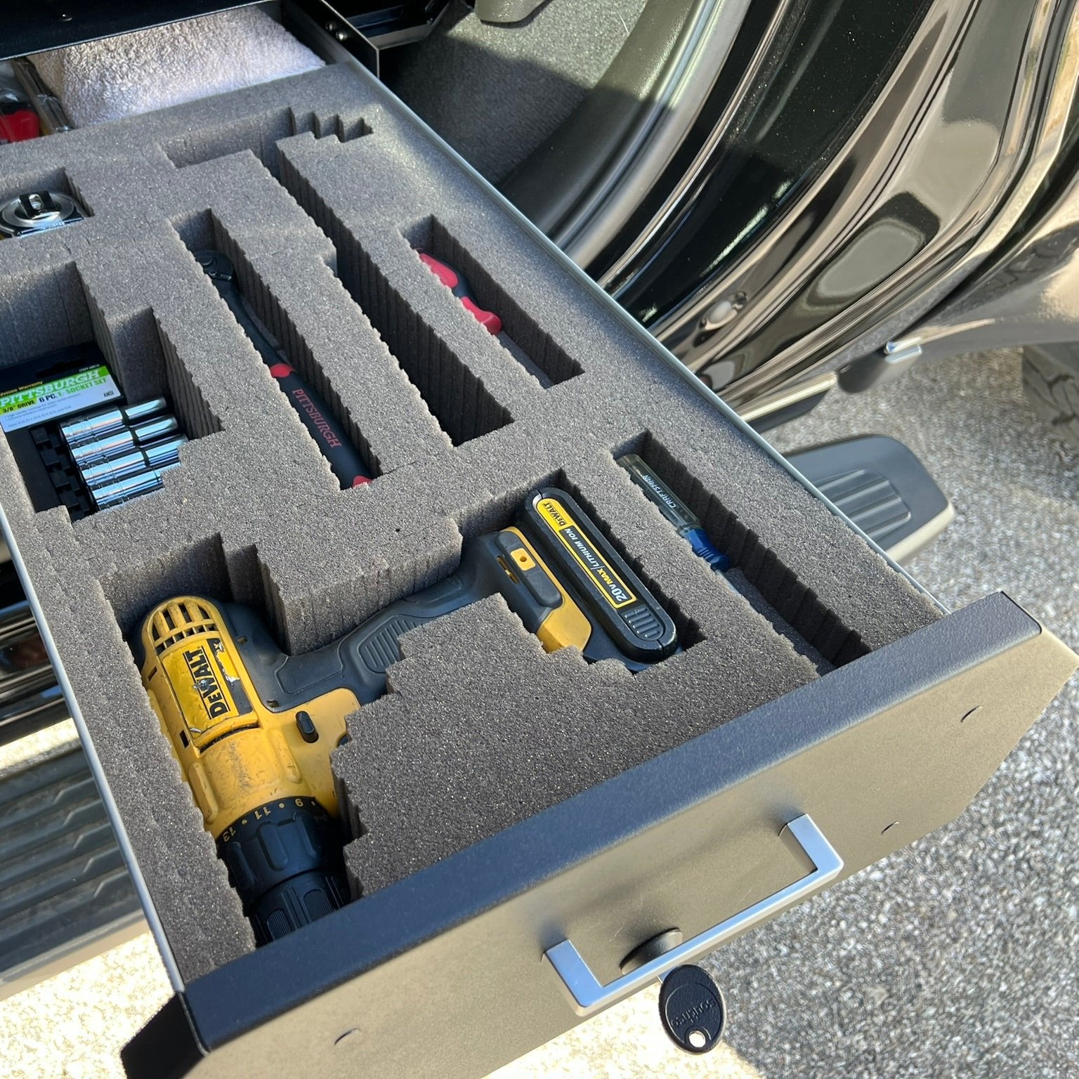 Chevy/GMC Gear-Guard Under-Seat Locker with the door open with the foam option that highlights tools placed in the foam and installed in a truck. The locker is a high-quality powder coated galvanized steel.